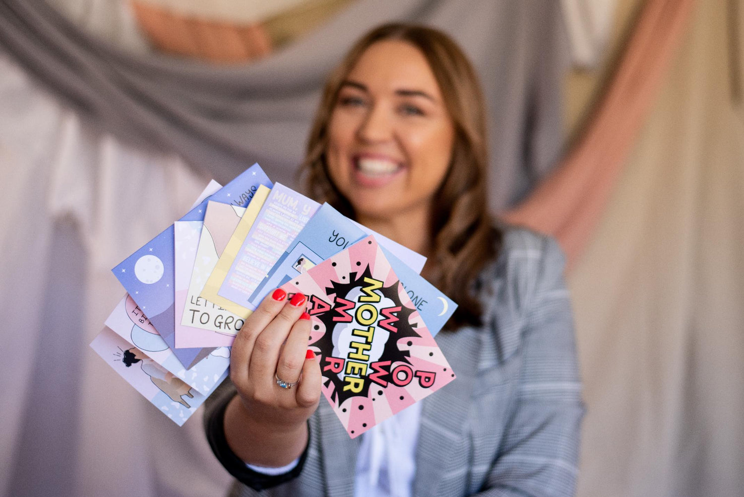 Founder of Motherhood Milestones, Emily Mitchell, smiling at the camera and holding up her Motherhood Milestones magnetic greeting cards. 