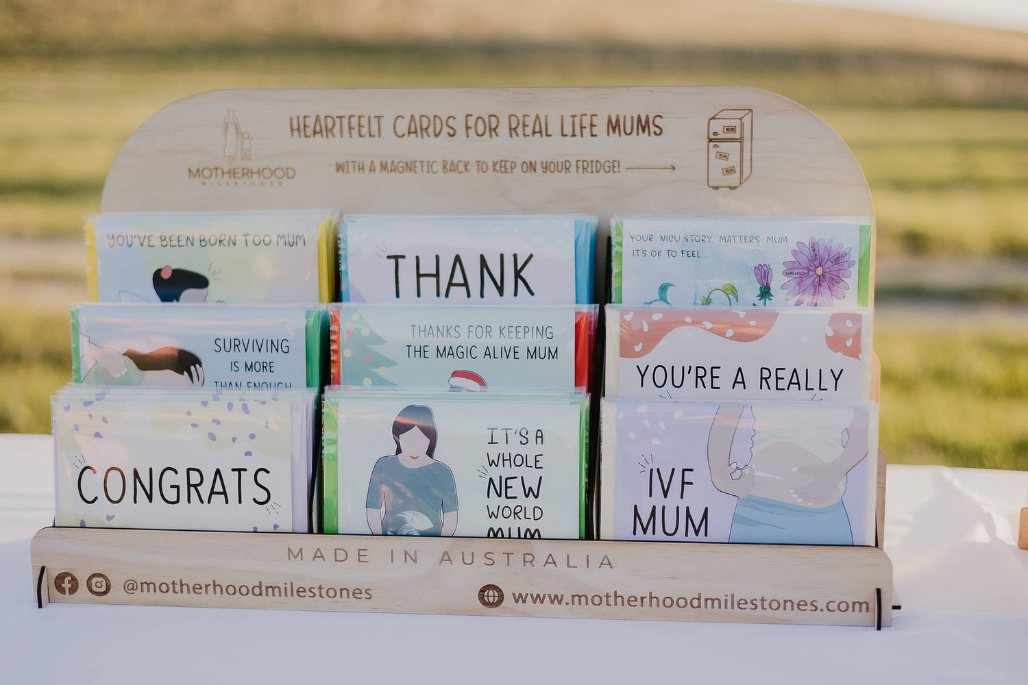 A Motherhood Milestones wooden stockist card stand filled with Motherhood Milestones card. There are nine sections for a cards and a header board that reads Heartfelt cards for real life mums with a magnetic back to live on your fridge.