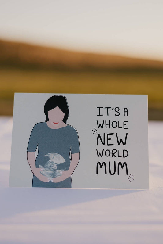 Image of the front of a Motherhood Milestones card that reads it's a whole new world mum. This card celebrates pregnancy and the mothers experience. There is an image of a woman cradling her stomach with a sonogram picture over her belly that looks the world, made with blue and green colours. She is wearing a dark green dress and the background of the card is light green.