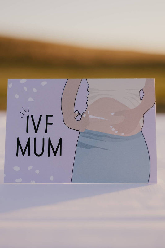The front of a Motherhood Milestones Card with a woman holding a needle at her stomach and the words next to her say IVF mum celebrating mothers on a fertility journey. The background is purple.