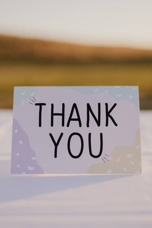 An image of a card that reads thank you. It has colours in each corner, green, blue, purple and yellow with white splotches.